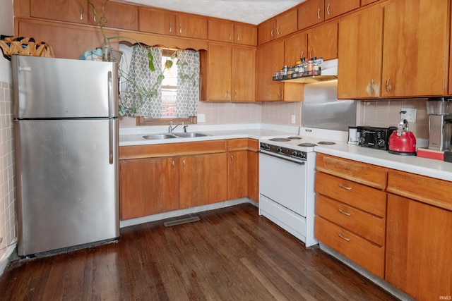 kitchen with white electric stove, light countertops, brown cabinetry, freestanding refrigerator, and a sink