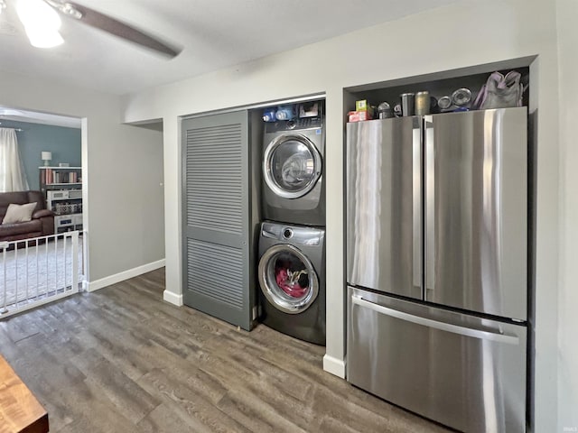 clothes washing area featuring wood finished floors, baseboards, and stacked washer and dryer