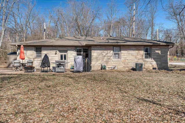 rear view of house with a shingled roof, central AC unit, stone siding, and a lawn