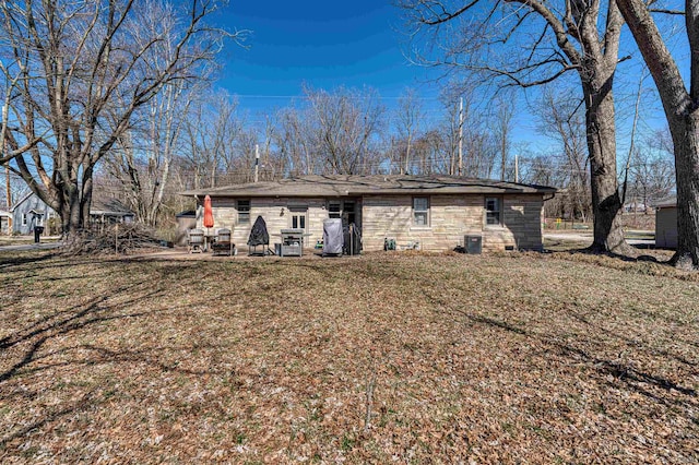 back of house with stone siding, a lawn, and central AC