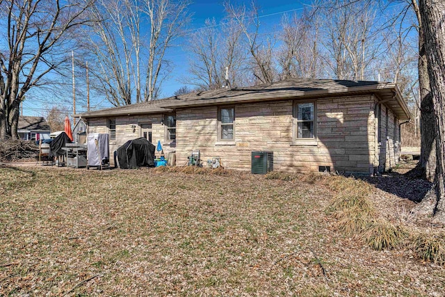 back of property featuring central air condition unit, stone siding, and a lawn