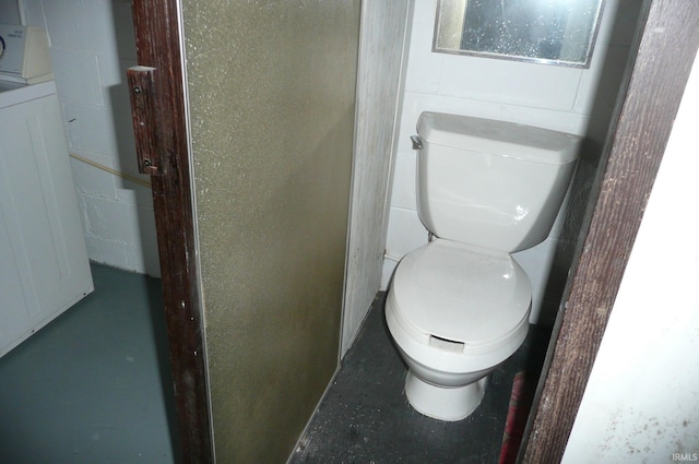 bathroom featuring washer / dryer, concrete block wall, concrete floors, and toilet