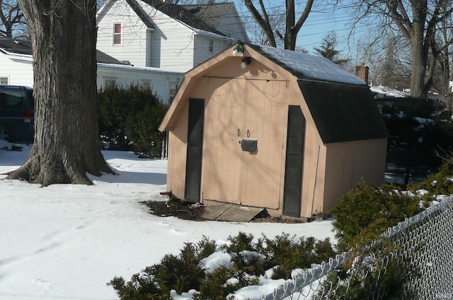 snow covered structure with a storage unit, fence, and an outdoor structure