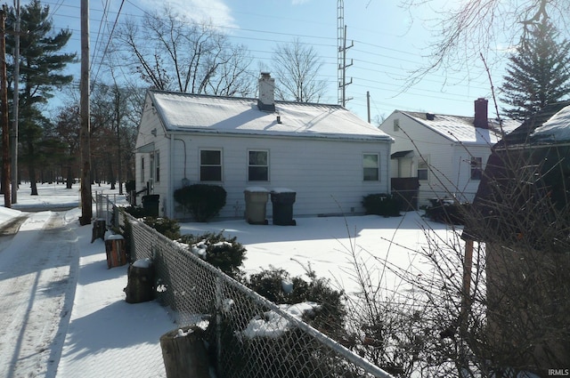 snow covered house featuring a chimney and fence