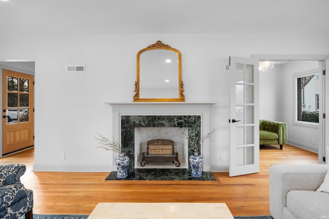 living area with baseboards, visible vents, wood finished floors, and a high end fireplace