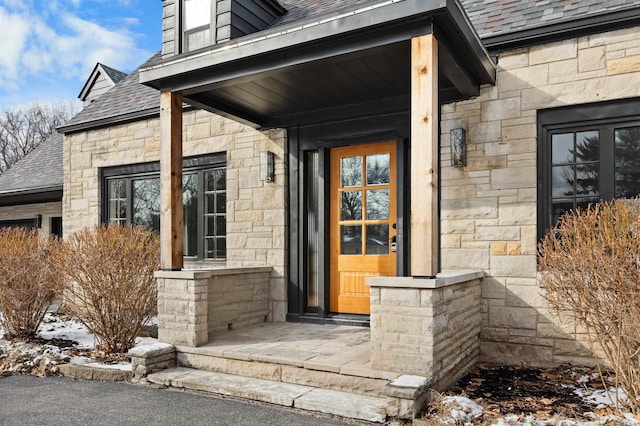 snow covered property entrance featuring stone siding and a shingled roof