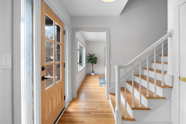 entryway featuring light wood finished floors, baseboards, and stairway