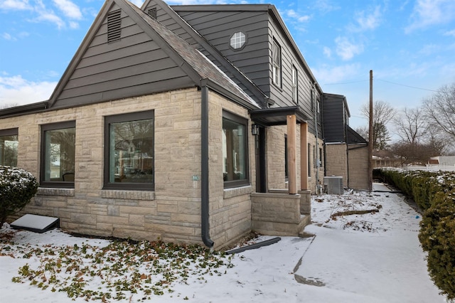 snow covered property featuring stone siding and central AC