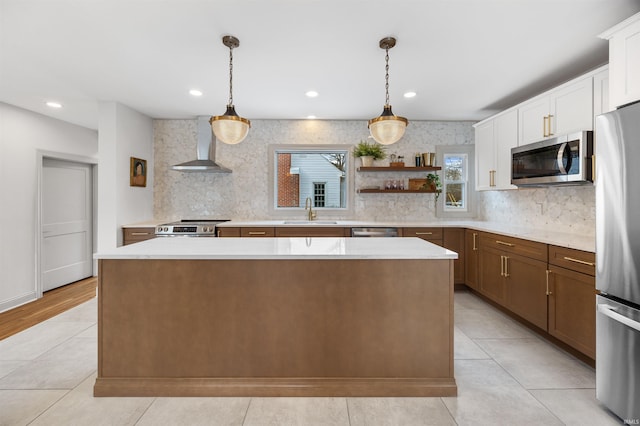 kitchen featuring stainless steel appliances, wall chimney range hood, light countertops, and decorative light fixtures