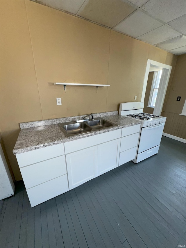 kitchen with white range with gas stovetop, white cabinets, a drop ceiling, light countertops, and a sink