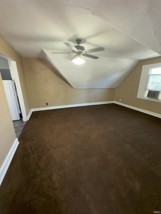 bonus room with a textured ceiling, a ceiling fan, baseboards, vaulted ceiling, and dark carpet