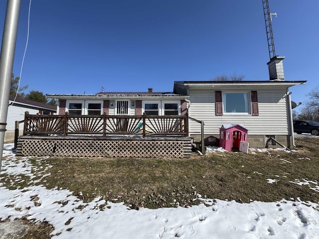 snow covered back of property with a yard, a chimney, and a wooden deck