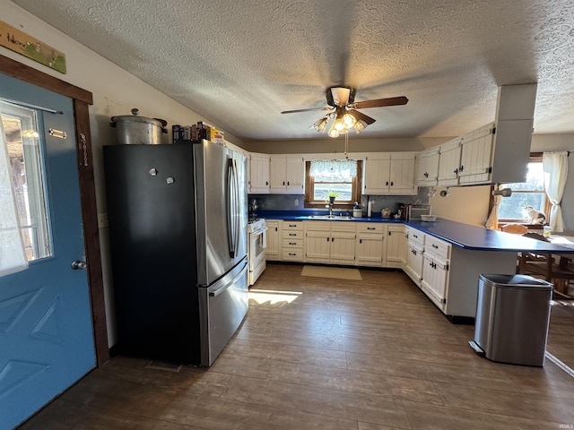 kitchen with white cabinets, dark countertops, dark wood-type flooring, freestanding refrigerator, and a sink