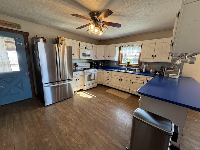 kitchen with dark countertops, dark wood-type flooring, white cabinets, a sink, and white appliances