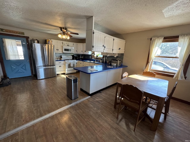 kitchen with white appliances, white cabinets, dark countertops, dark wood-style floors, and a peninsula