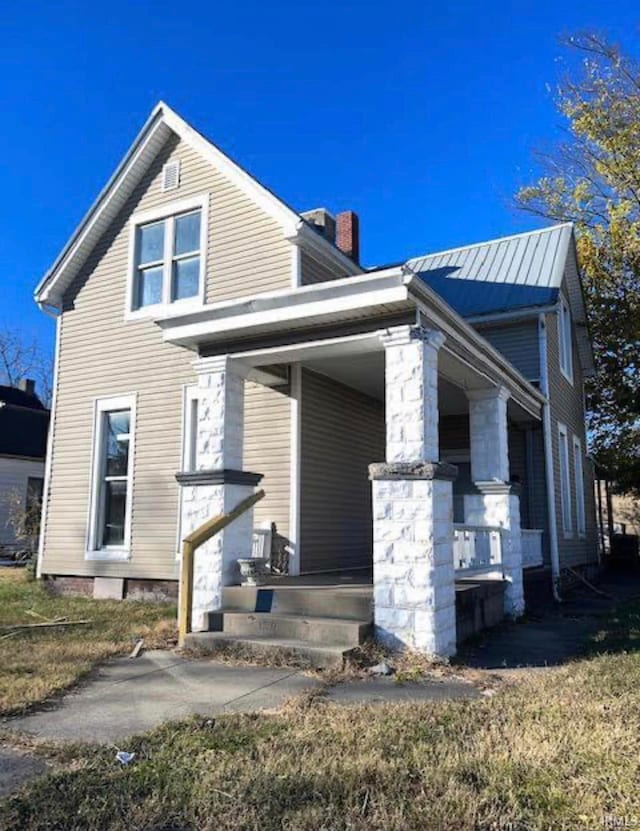 view of property exterior with covered porch, metal roof, and a chimney