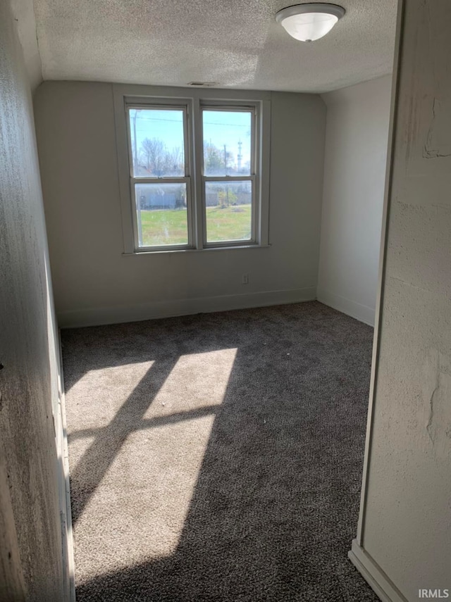 spare room with a textured ceiling, dark colored carpet, and baseboards