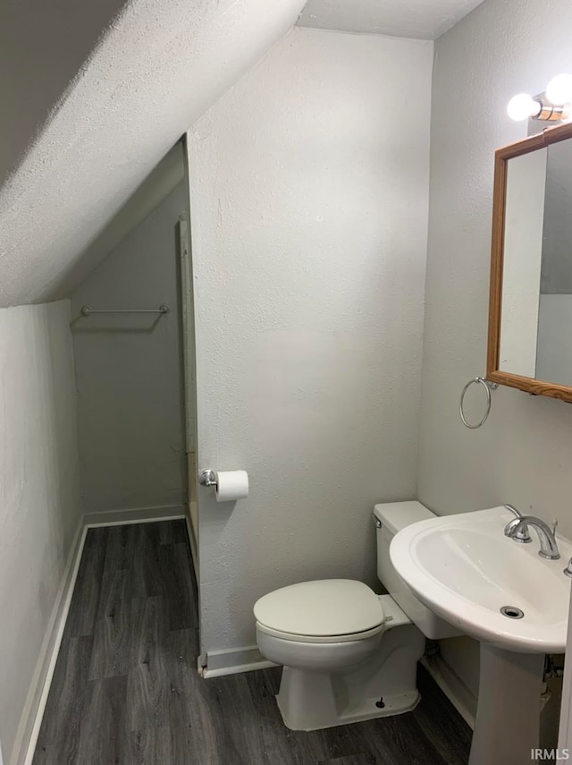 half bath with baseboards, toilet, lofted ceiling, wood finished floors, and a textured ceiling