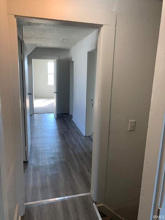 hallway with dark wood-style floors, a textured ceiling, and baseboards