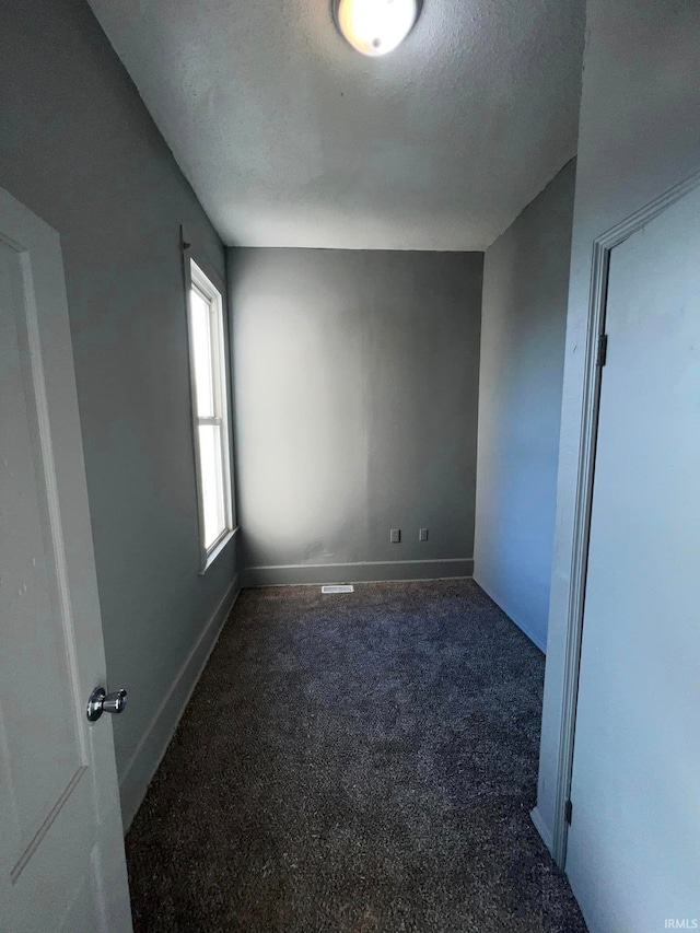 unfurnished room with a textured ceiling, dark colored carpet, and baseboards