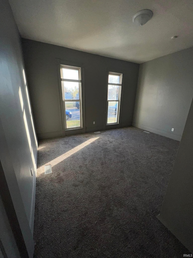 empty room with dark carpet, visible vents, and baseboards