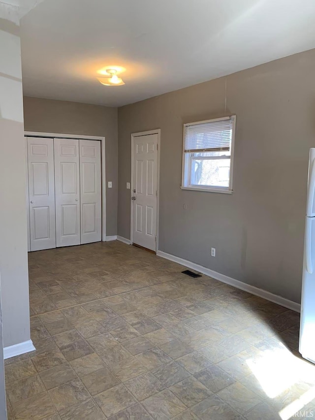 unfurnished bedroom with visible vents, baseboards, a closet, freestanding refrigerator, and stone finish floor