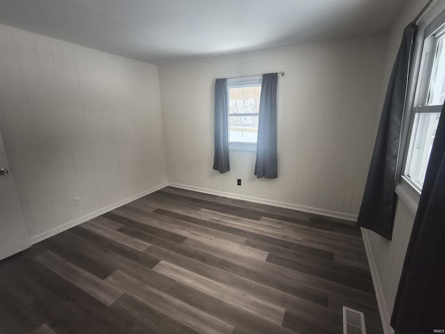 spare room with dark wood-style floors, visible vents, and baseboards