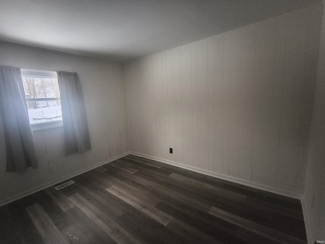 spare room with dark wood-style flooring, visible vents, and baseboards