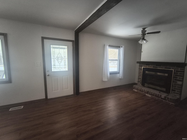 unfurnished living room with dark wood-type flooring, a brick fireplace, visible vents, and a ceiling fan