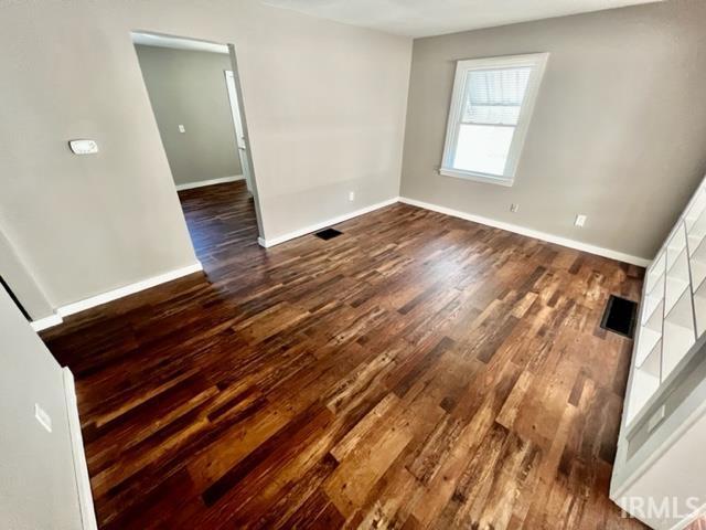 unfurnished room with dark wood-type flooring, visible vents, and baseboards