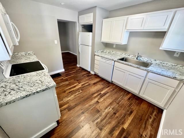 kitchen with white appliances, a sink, baseboards, white cabinets, and dark wood-style floors