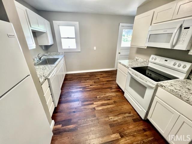 kitchen with dark wood finished floors, white cabinets, a sink, white appliances, and baseboards