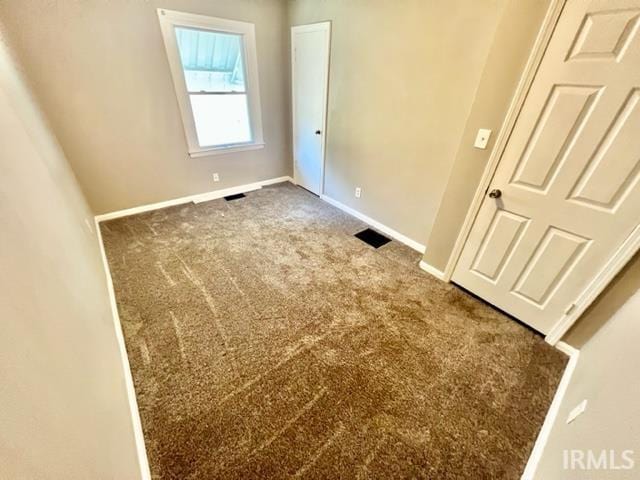 unfurnished bedroom with visible vents, dark carpet, and baseboards