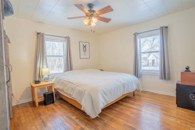 bedroom with ceiling fan, multiple windows, baseboards, and wood finished floors