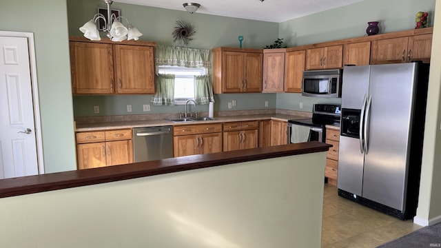 kitchen with appliances with stainless steel finishes, brown cabinetry, a sink, and an inviting chandelier