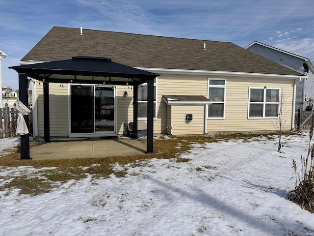 snow covered property with a shingled roof, a patio, and a gazebo