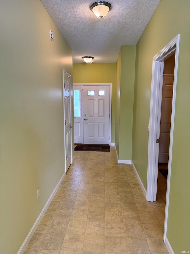 doorway to outside featuring baseboards and a textured ceiling