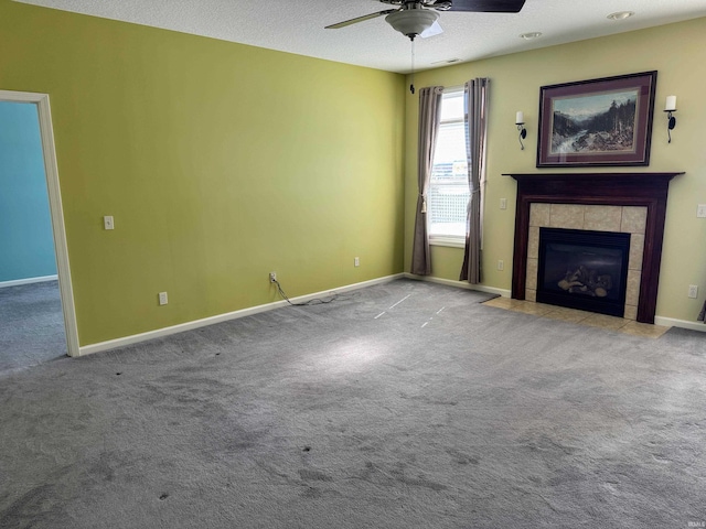 unfurnished living room with carpet floors, a tile fireplace, ceiling fan, and baseboards