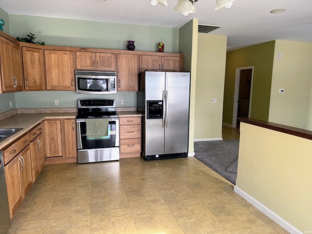 kitchen featuring baseboards, visible vents, brown cabinets, stainless steel appliances, and a textured ceiling