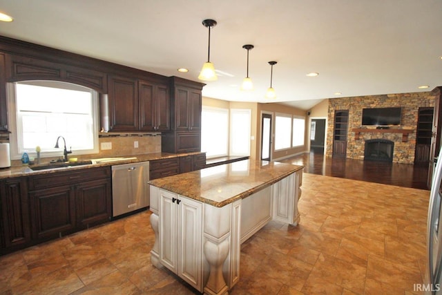 kitchen with a kitchen island, light stone counters, hanging light fixtures, a sink, and stainless steel dishwasher