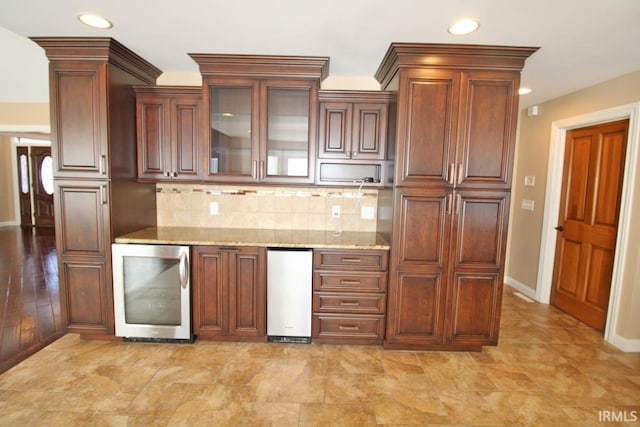 kitchen with light stone countertops, wine cooler, glass insert cabinets, and backsplash