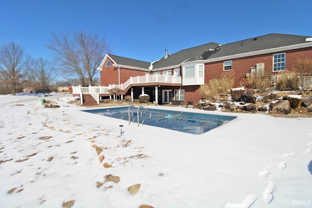 snow covered pool with a deck, stairway, and an outdoor pool