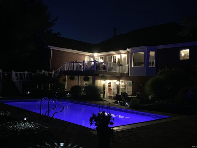 pool at twilight with an outdoor pool, a deck, and stairs