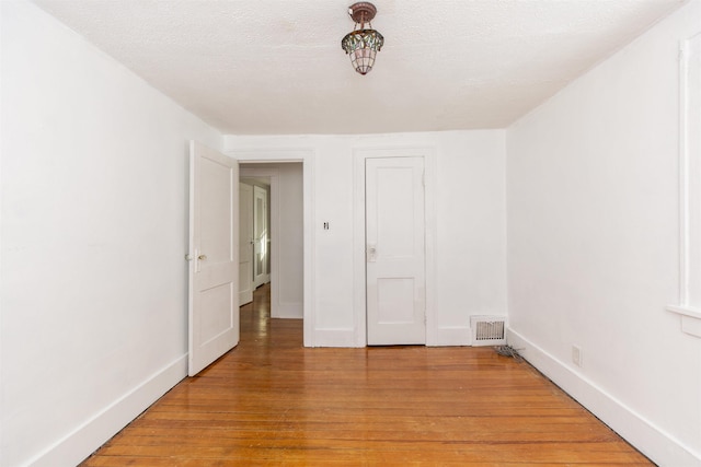 unfurnished room featuring light wood-type flooring, baseboards, visible vents, and a textured ceiling