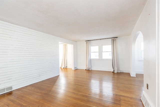 spare room with light wood-style floors, visible vents, arched walkways, and a textured ceiling