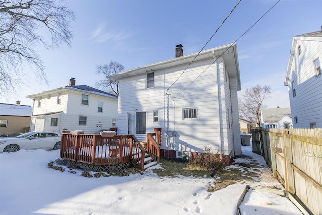 snow covered house featuring a chimney, fence, and a deck