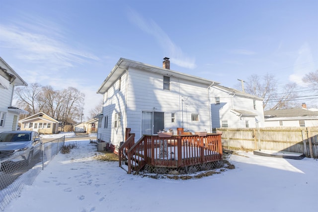 snow covered rear of property with fence, a chimney, and a wooden deck