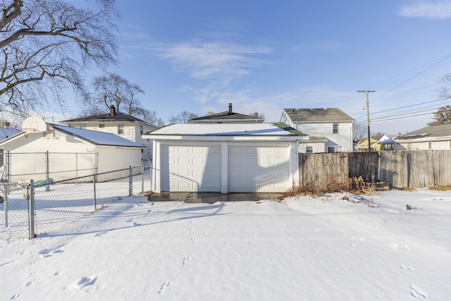 snow covered rear of property featuring an outdoor structure, fence, and a detached garage