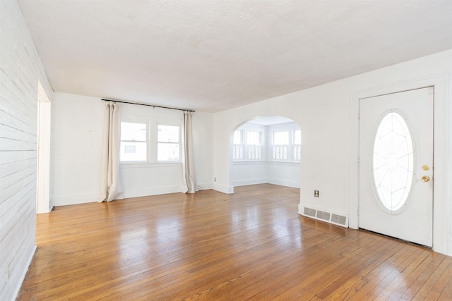 foyer entrance with baseboards, visible vents, arched walkways, a textured ceiling, and light wood-type flooring