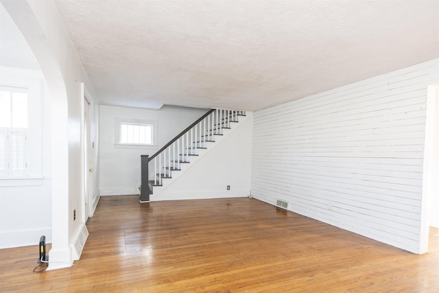 unfurnished living room with visible vents, stairway, a textured ceiling, and wood finished floors